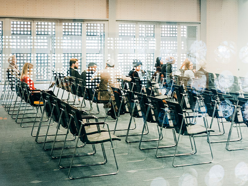 Looking through glass wall of meeting room, people gathering in seats facing toward front